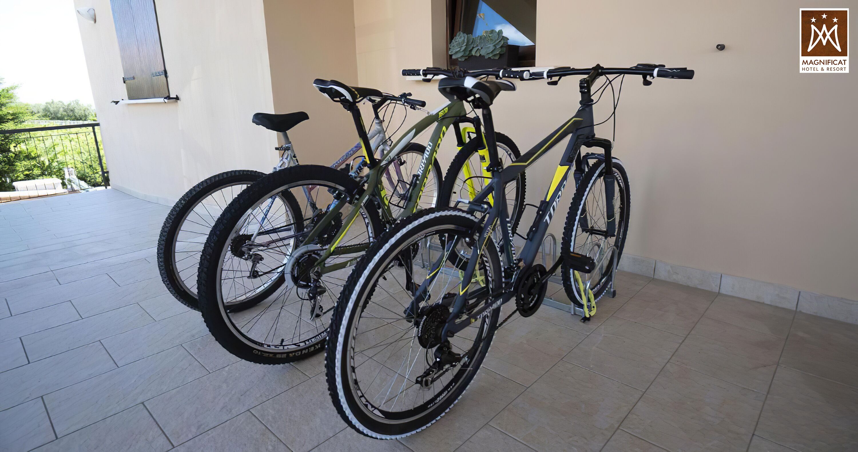 Deux vélos sont garés sur un balcon carrelé, avec en arrière-plan une vue sur la verdure.