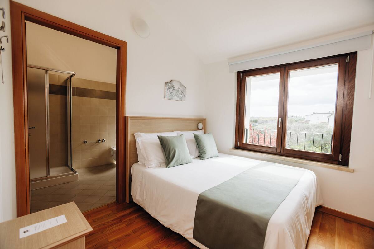 Un dormitorio con cama, ventana con vistas, suelo de madera y zona de ducha.