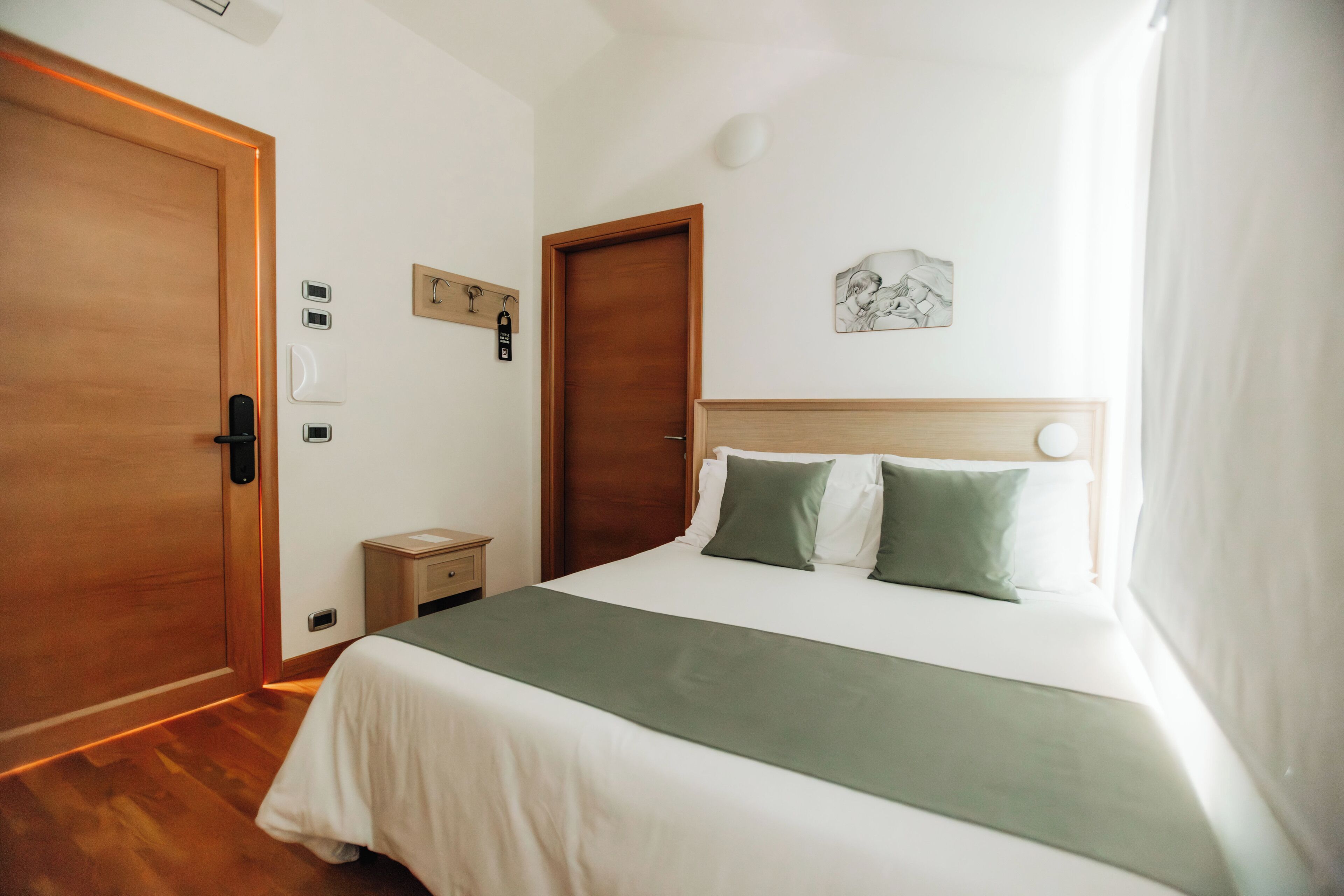 A hotel room with a bed, wooden doors, a nightstand, a wall clock, and a small picture.