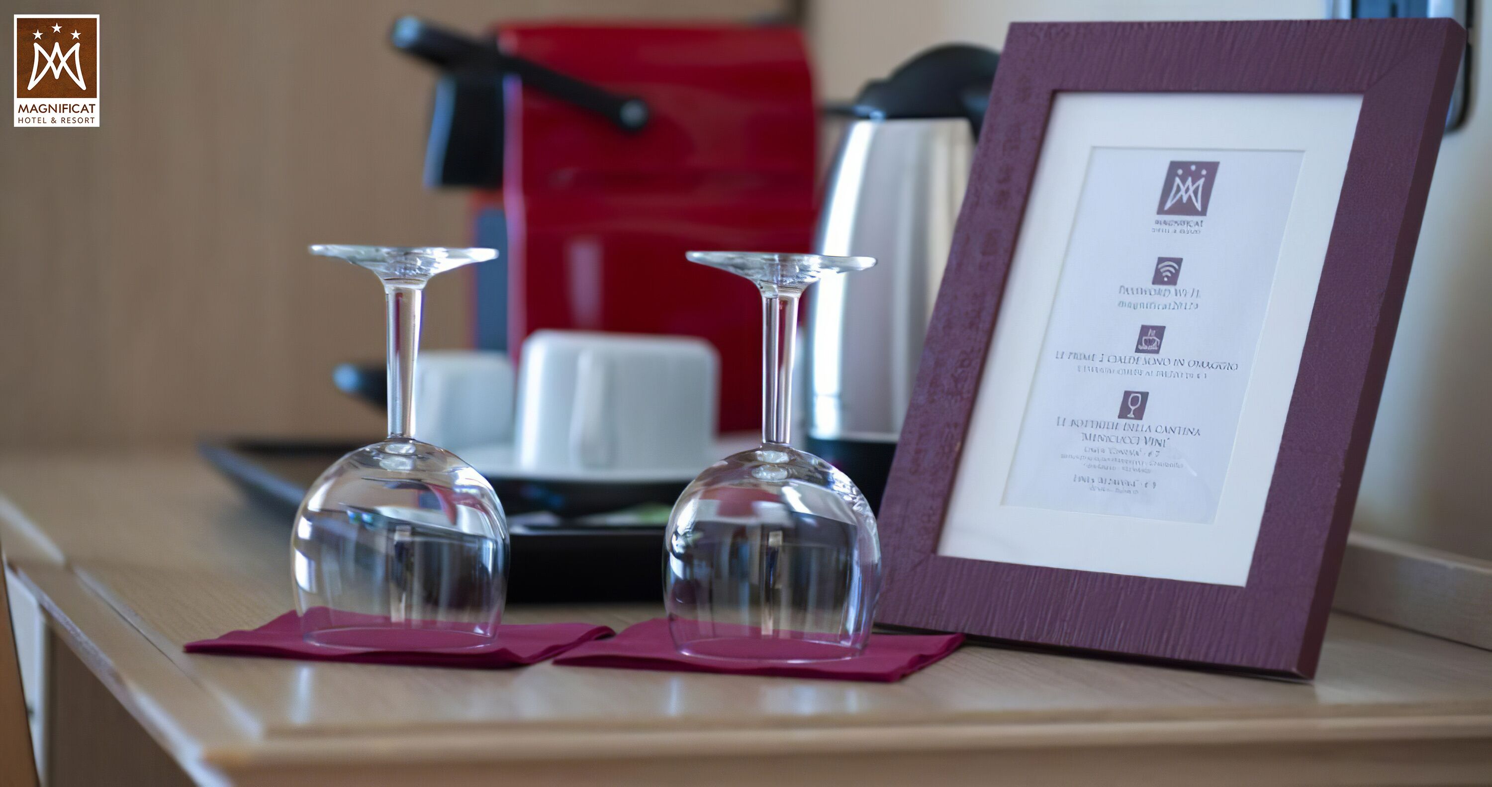 A framed menu on a table with two wine glasses on pink napkins.
