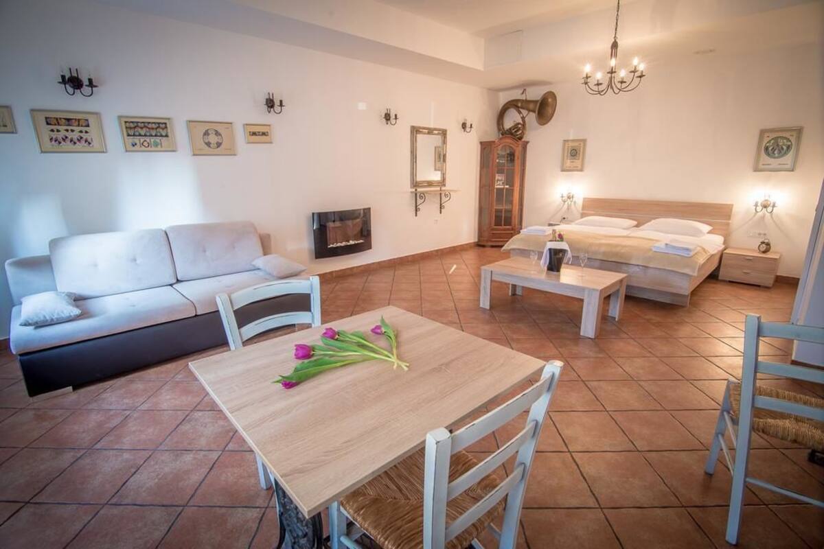 Een moderne woonkamer met een bank, een eettafel met stoelen, een houten salontafel, een bed en een kroonluchter.
