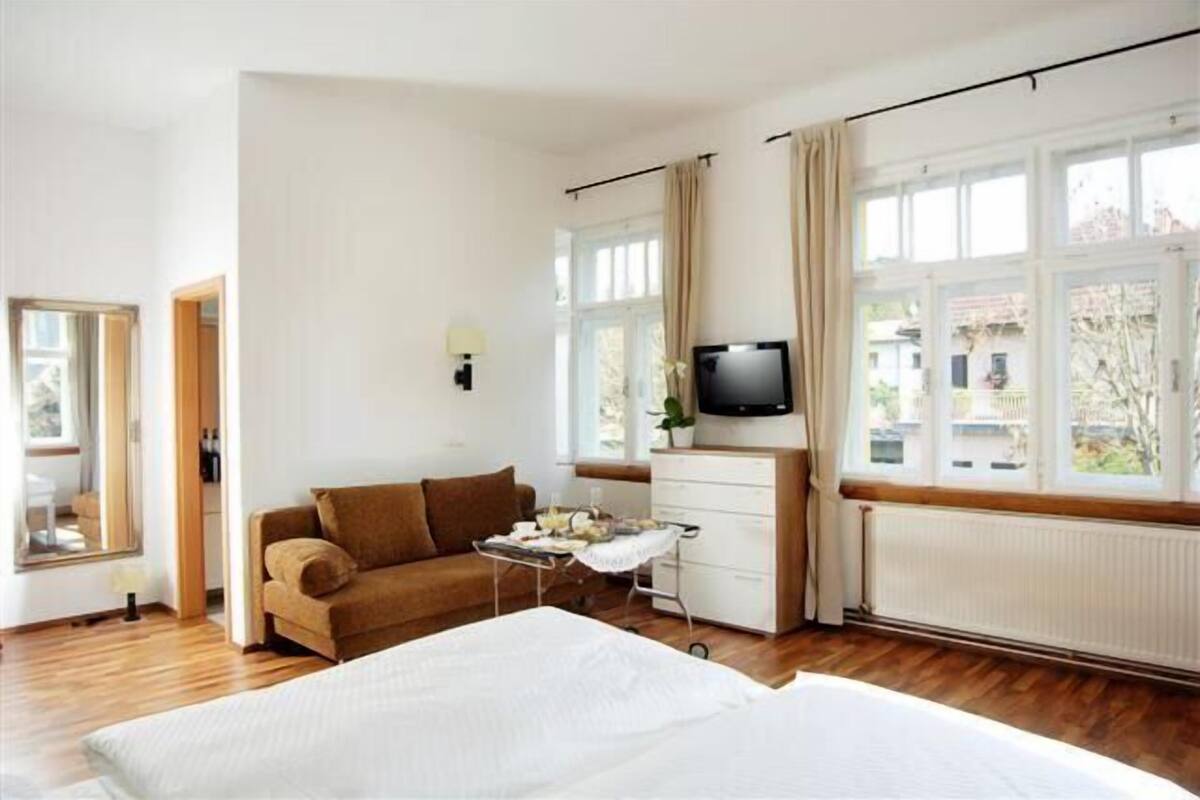 Een slaapkamer met een bed, een bank, een televisie, een raam en een radiator.