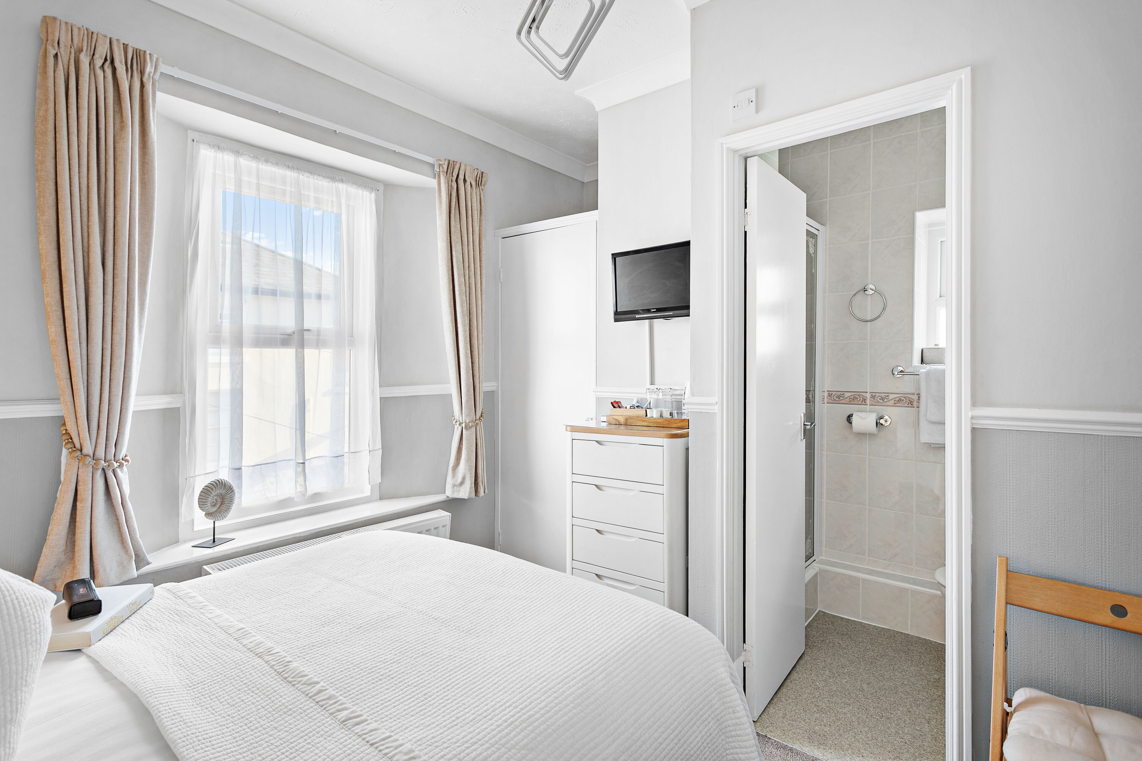 Habitación de hotel con cama, televisor, escritorio y silla, ducha y ventana con cortinas.