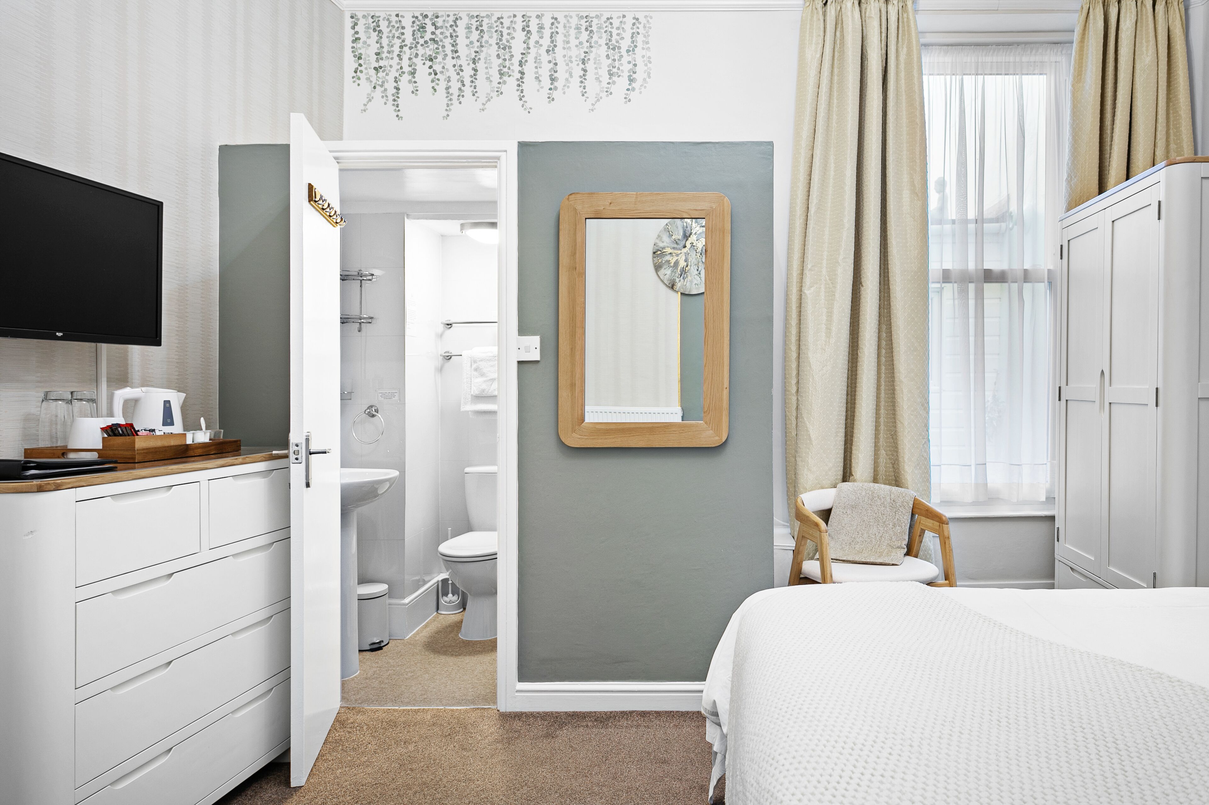 Habitación de hotel con cama, televisor, baño con inodoro y lavamanos, y armario.
