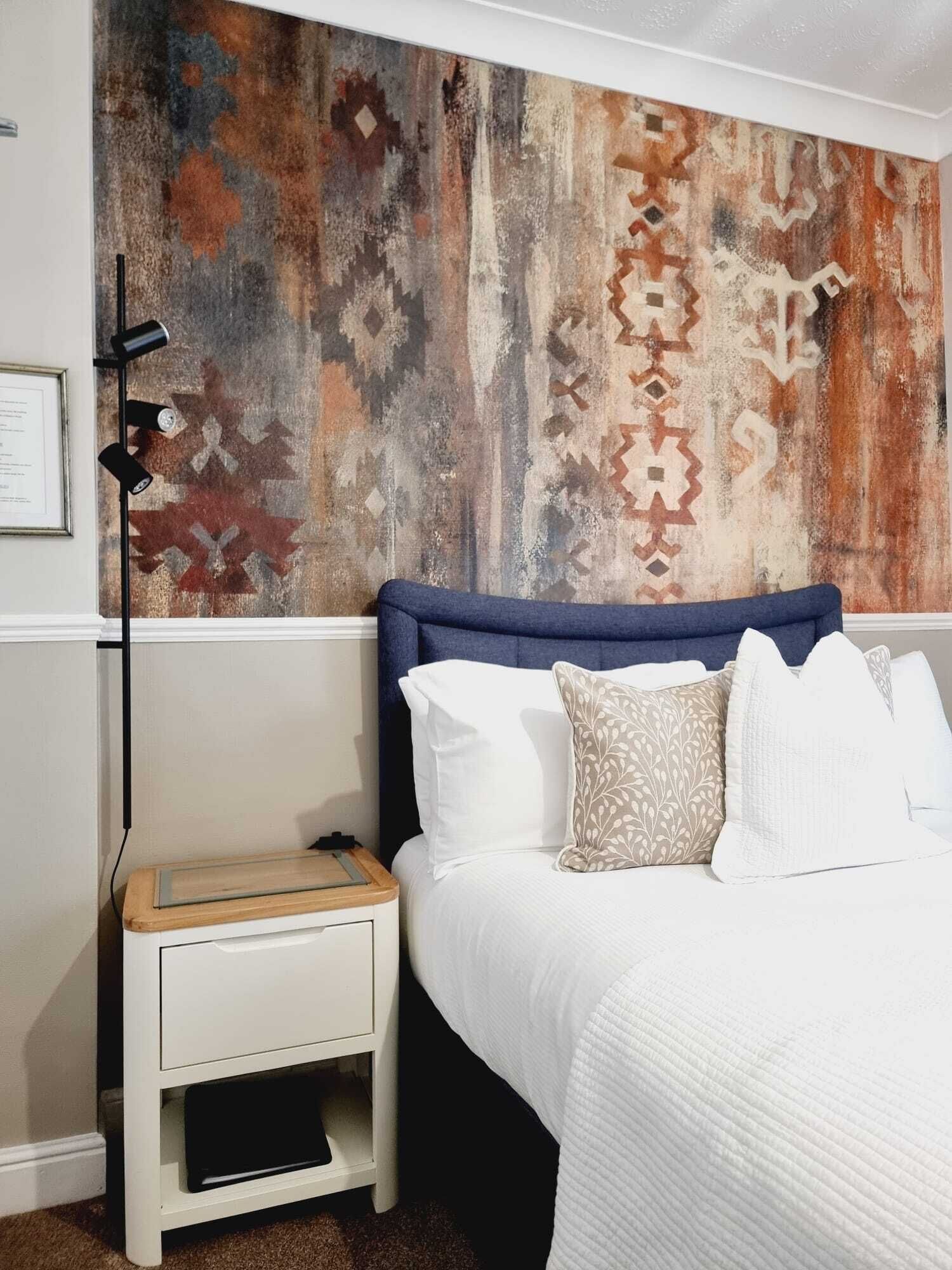 Un dormitorio con cama, mesita de noche blanca y pared con diseño.