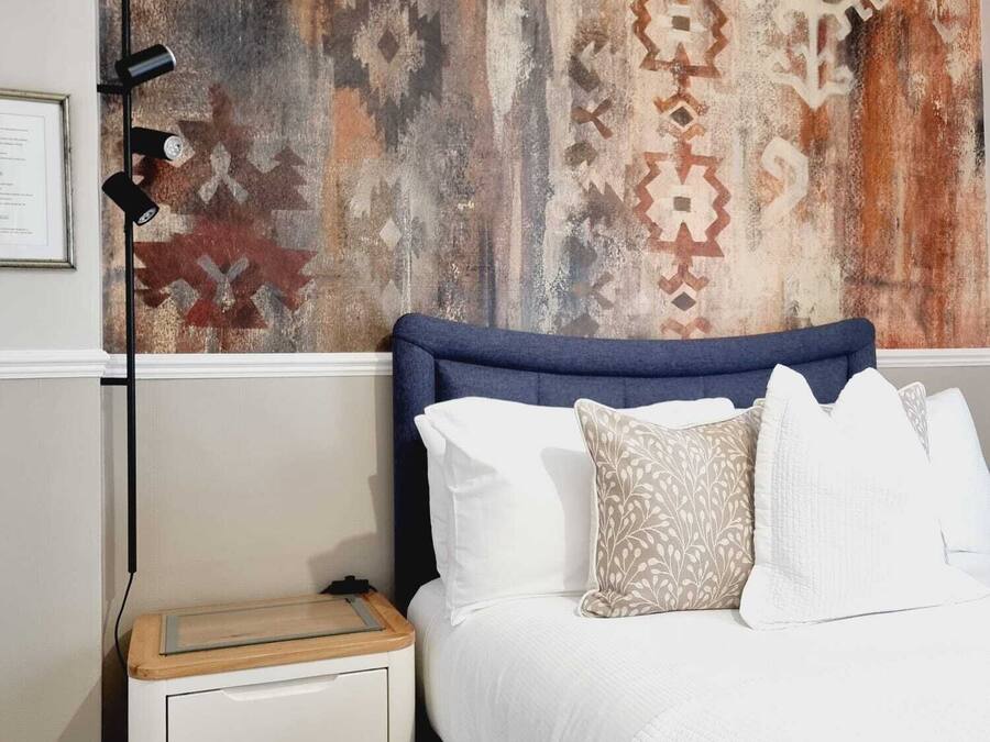 Un dormitorio con cama, mesita de noche blanca y pared con diseño.