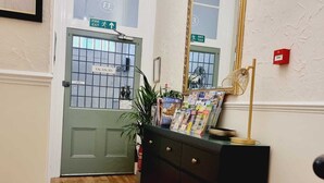 A hallway with a green door marked "VACANCIES," a mirror, a magazine rack, and a small plant.