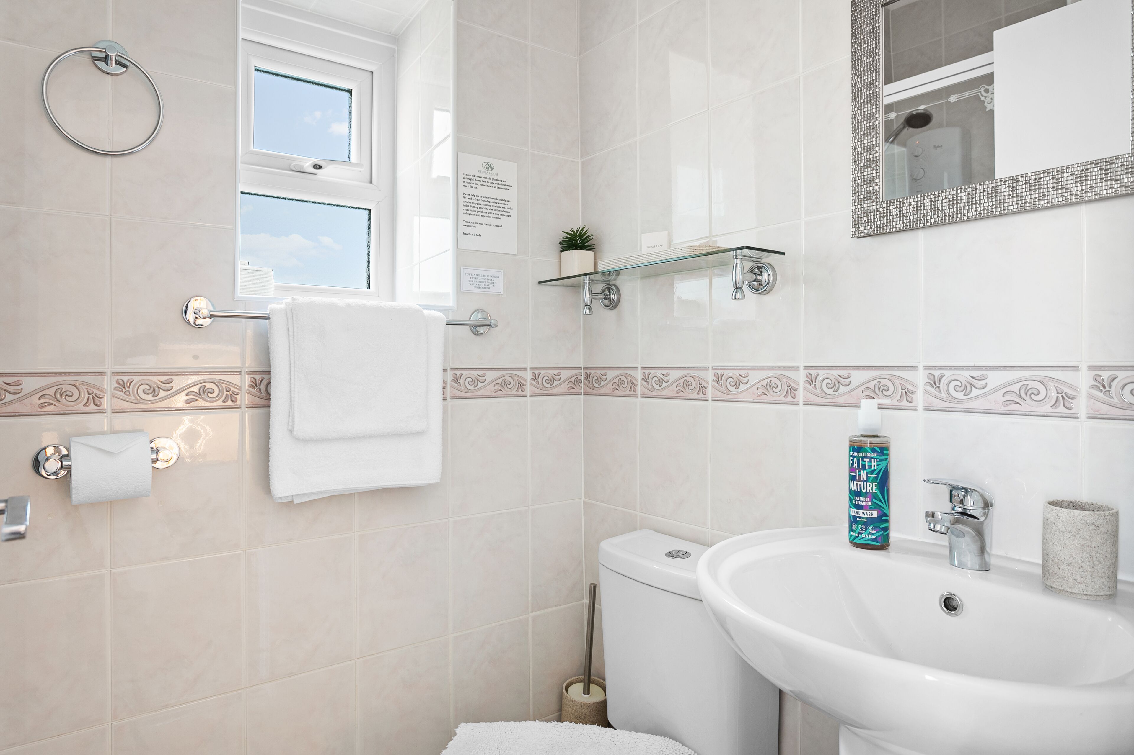A bathroom with a toilet, sink, towel rack, glass shelf, and a mirror.