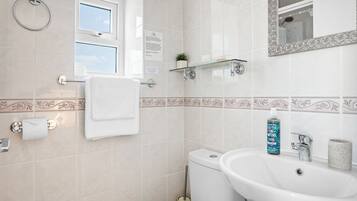 A bathroom with a toilet, sink, towel rack, glass shelf, and a mirror.