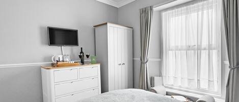 A bedroom with a bed, a TV mounted on the wall, a wardrobe, and a window with curtains.