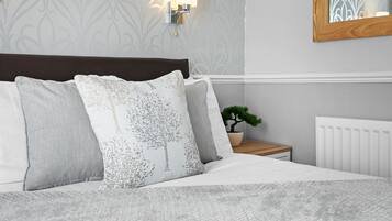 A neatly made bed with a white and gray patterned pillow, a small potted plant, and a wall-mounted light fixture.