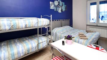 Ein Schlafsaalzimmer mit Etagenbetten, einem Schreibtisch, einem Stuhl, einer Topfpflanze, einer Fernbedienung und einem Fenster mit Vorhängen.