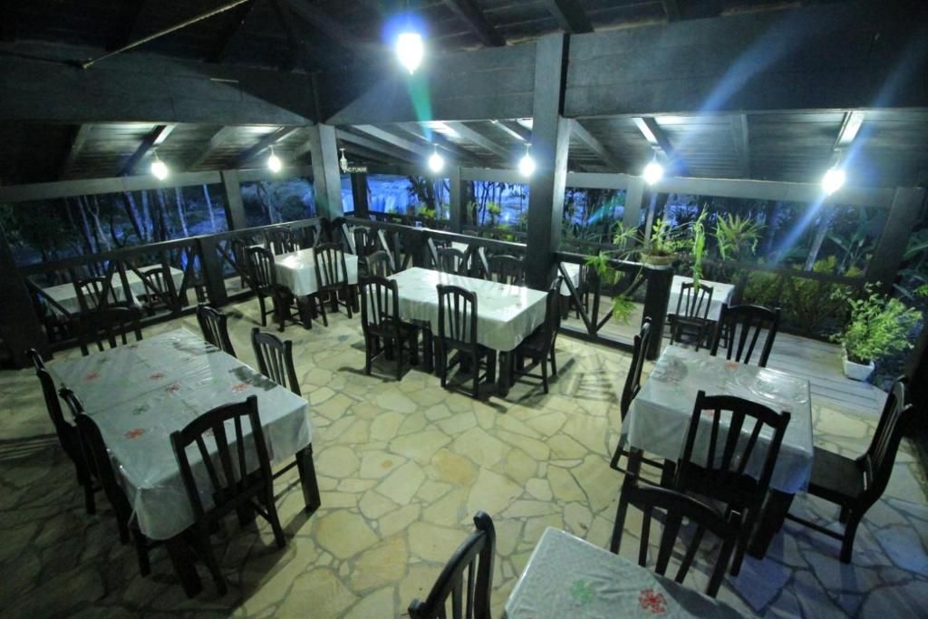 An outdoor dining area with tables and chairs, surrounded by stone flooring and potted plants.