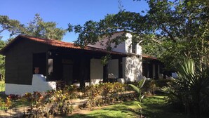 A building with a red-tiled roof, white walls, and a garden area with various plants and a palm tree. - Ecolodge Las Nubes Chiapas (Maravilla Tenejapa)