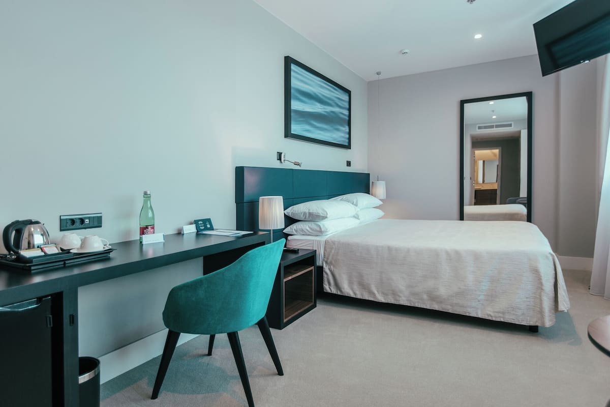 Una habitación de hotel moderna con cama, escritorio, silla y un espejo grande.