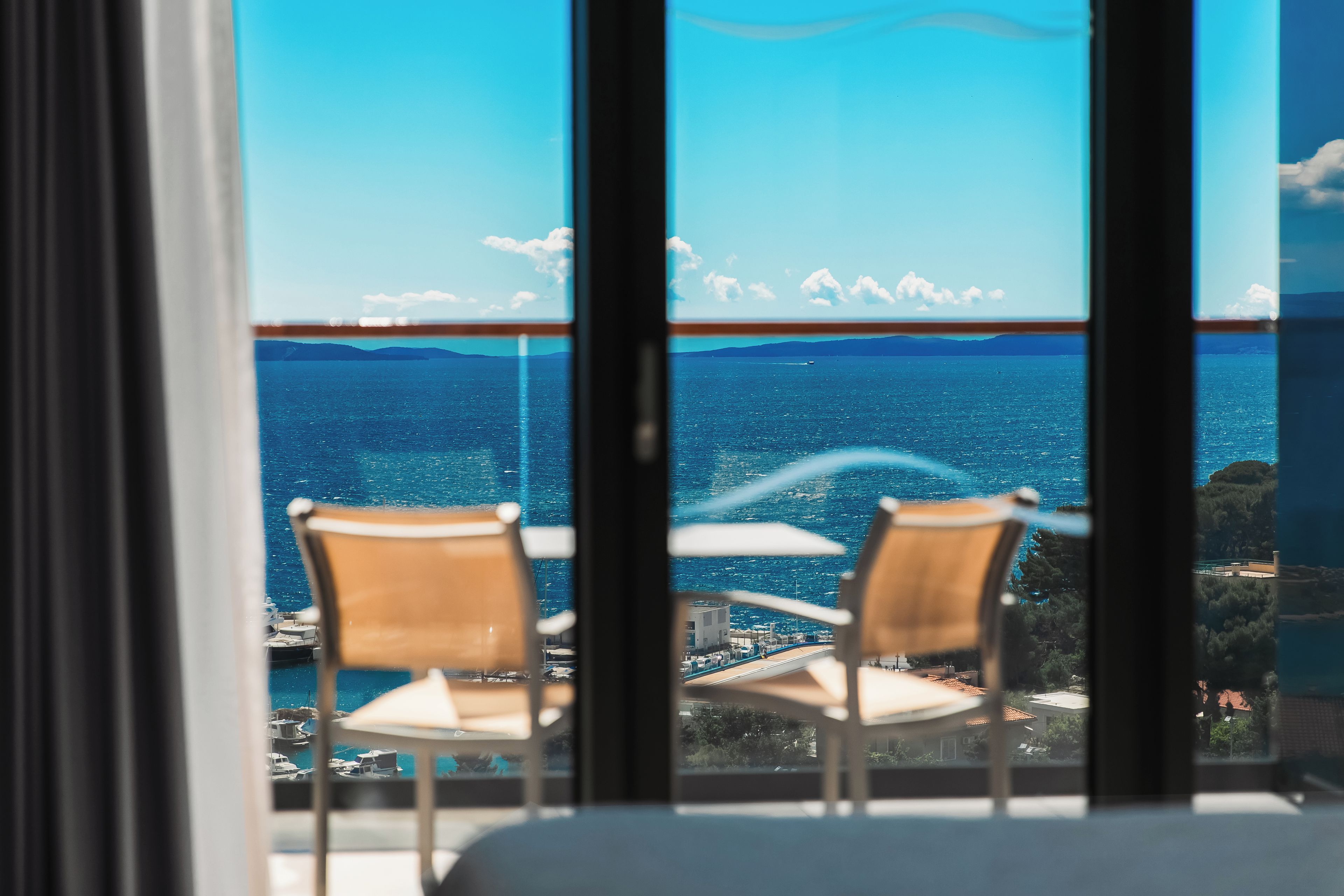 A balcony with two chairs and a table, overlooking a coastal view with boats and buildings.