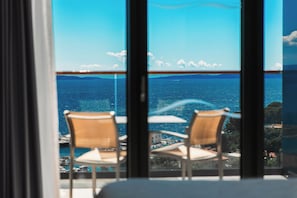 Un balcón con dos sillas y una mesa, con vistas a la costa, barcos y edificios.