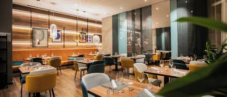 A modern restaurant with wooden flooring, yellow and grey chairs, and tables set for dining.