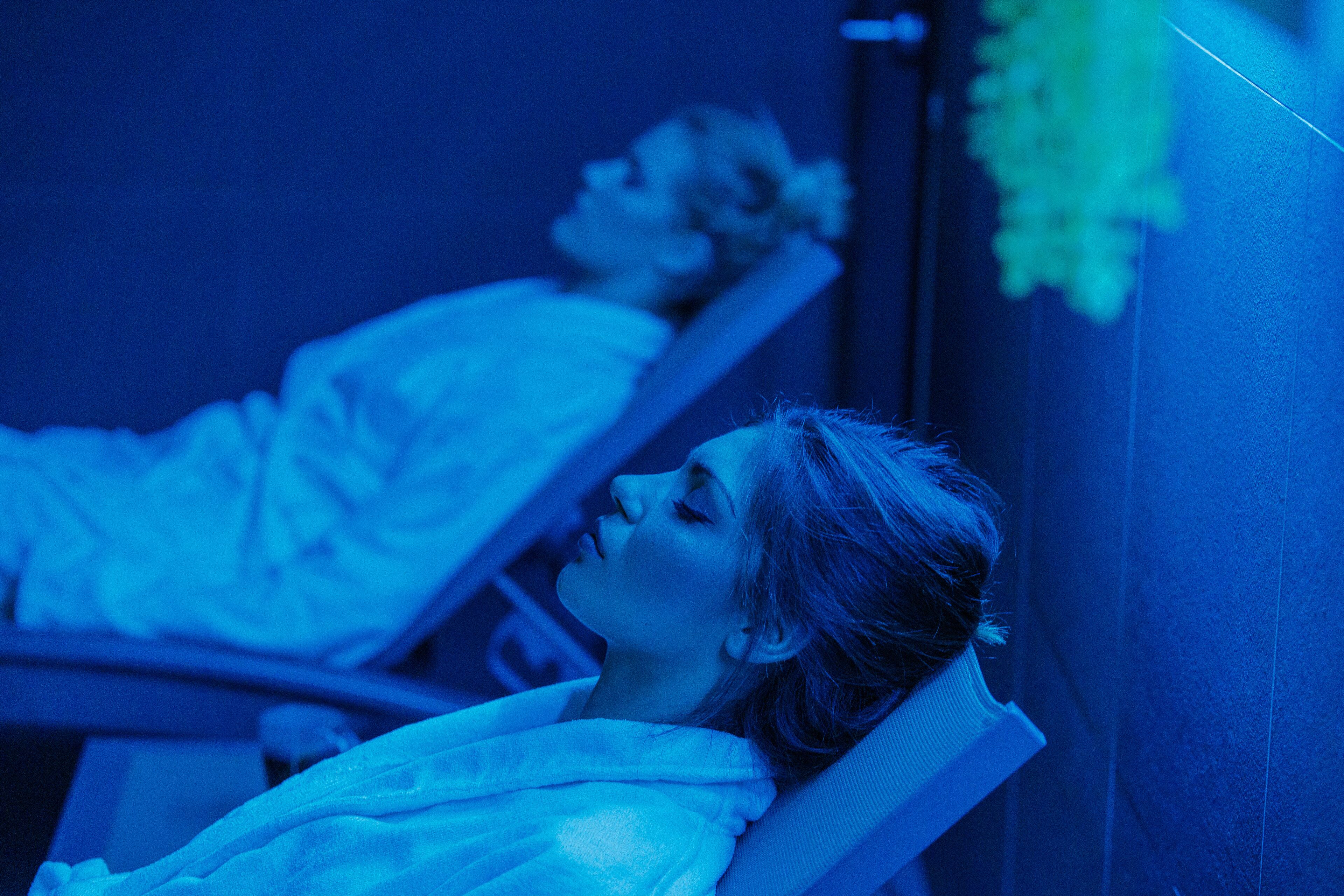 Una persona recostada en una cama dentro de una habitación con tonos azules.