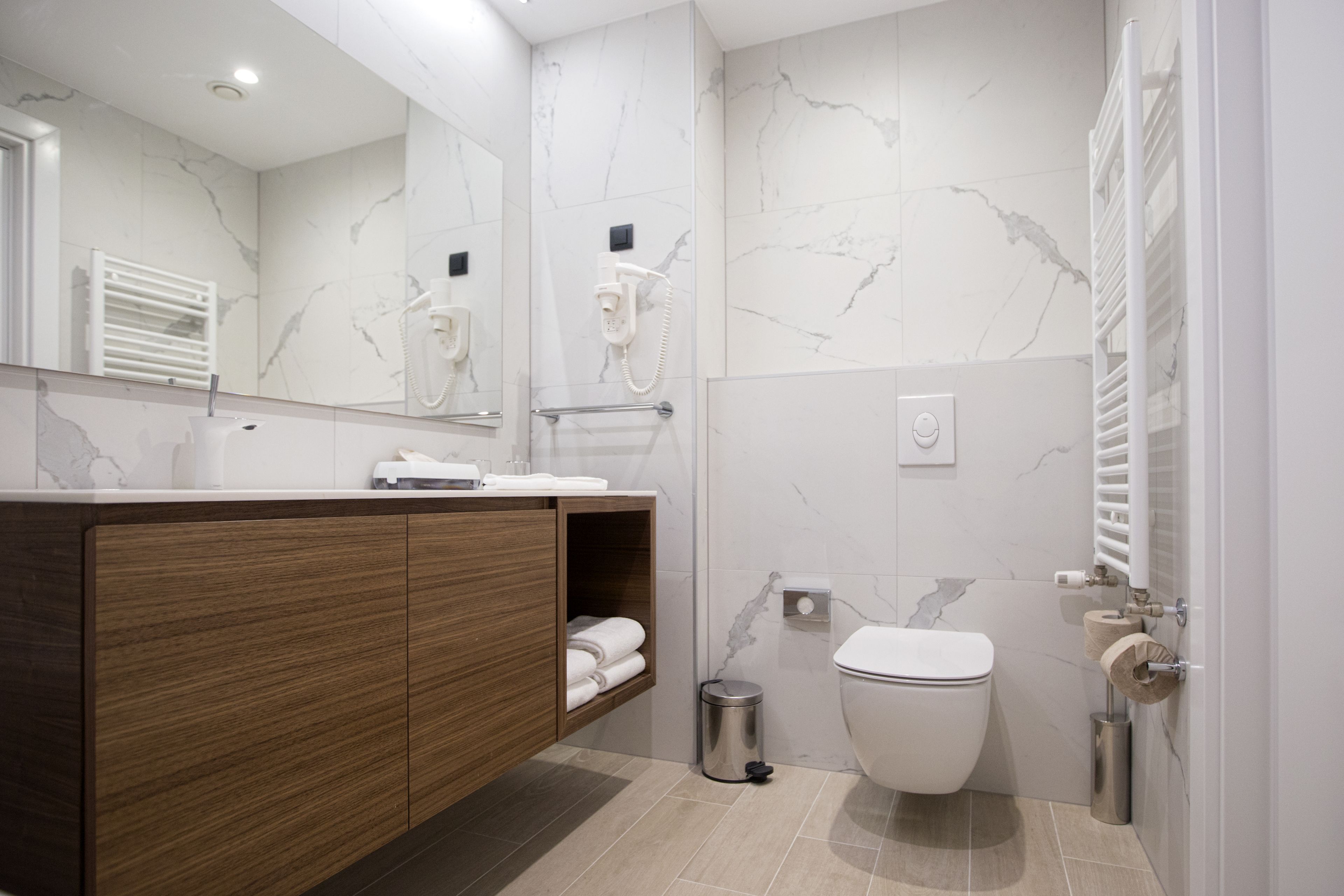 Une salle de bain moderne avec un mur en marbre, un meuble-lavabo en bois, des toilettes et un sèche-mains.