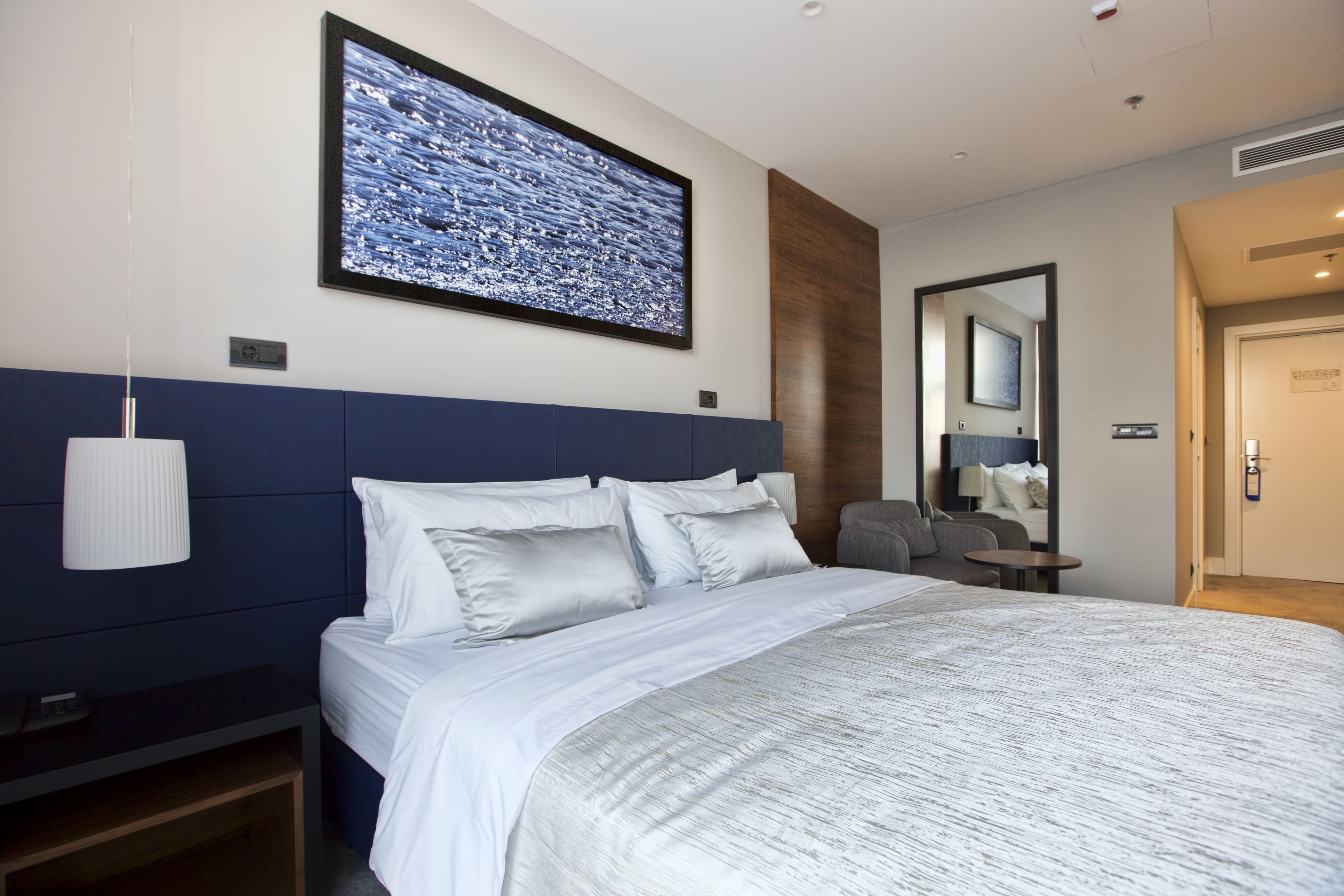 Una habitación de hotel moderna con una cama grande, un televisor de pared, una mesita de noche y un espejo.