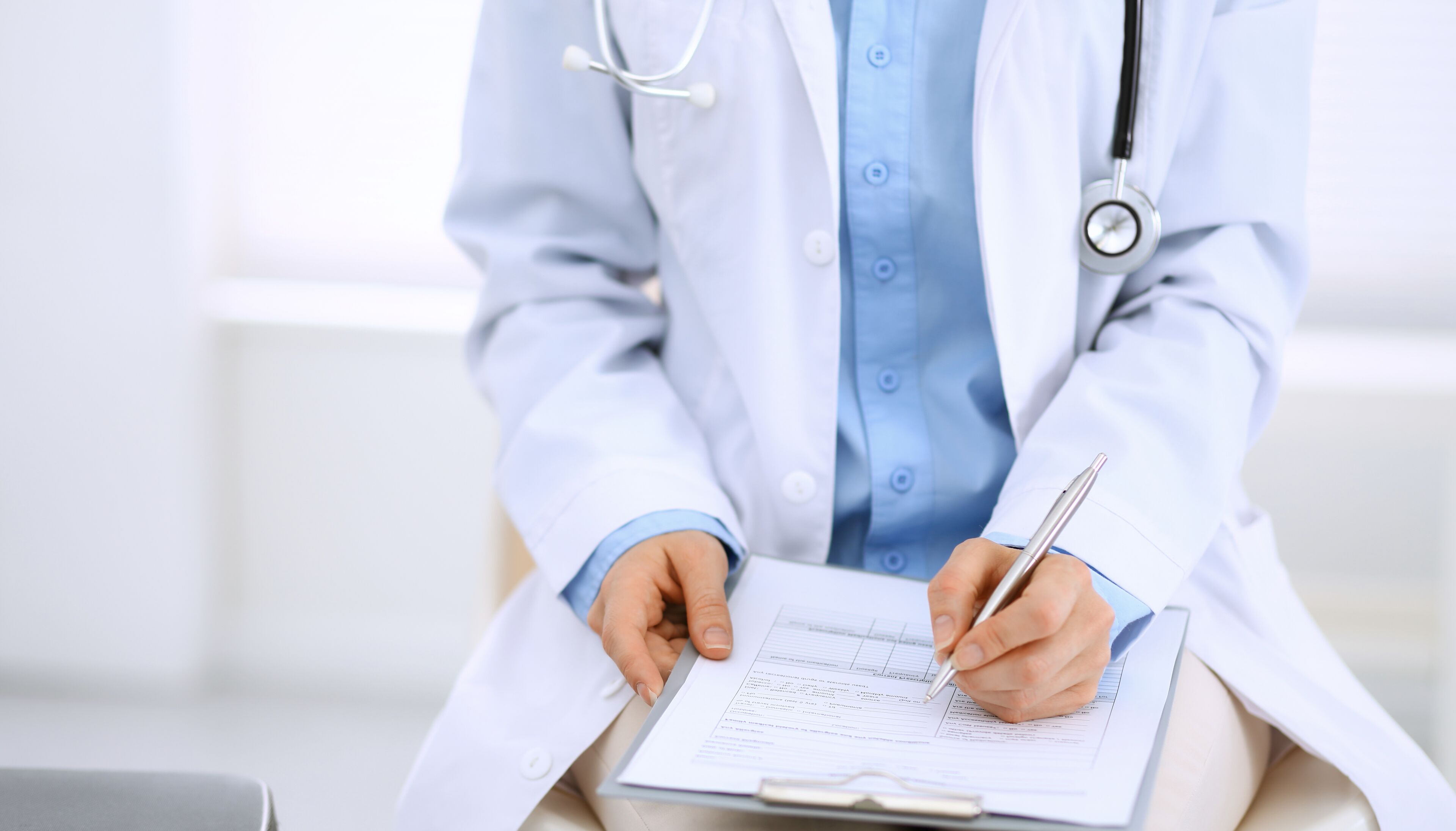 A person in a white lab coat writing on a clipboard.