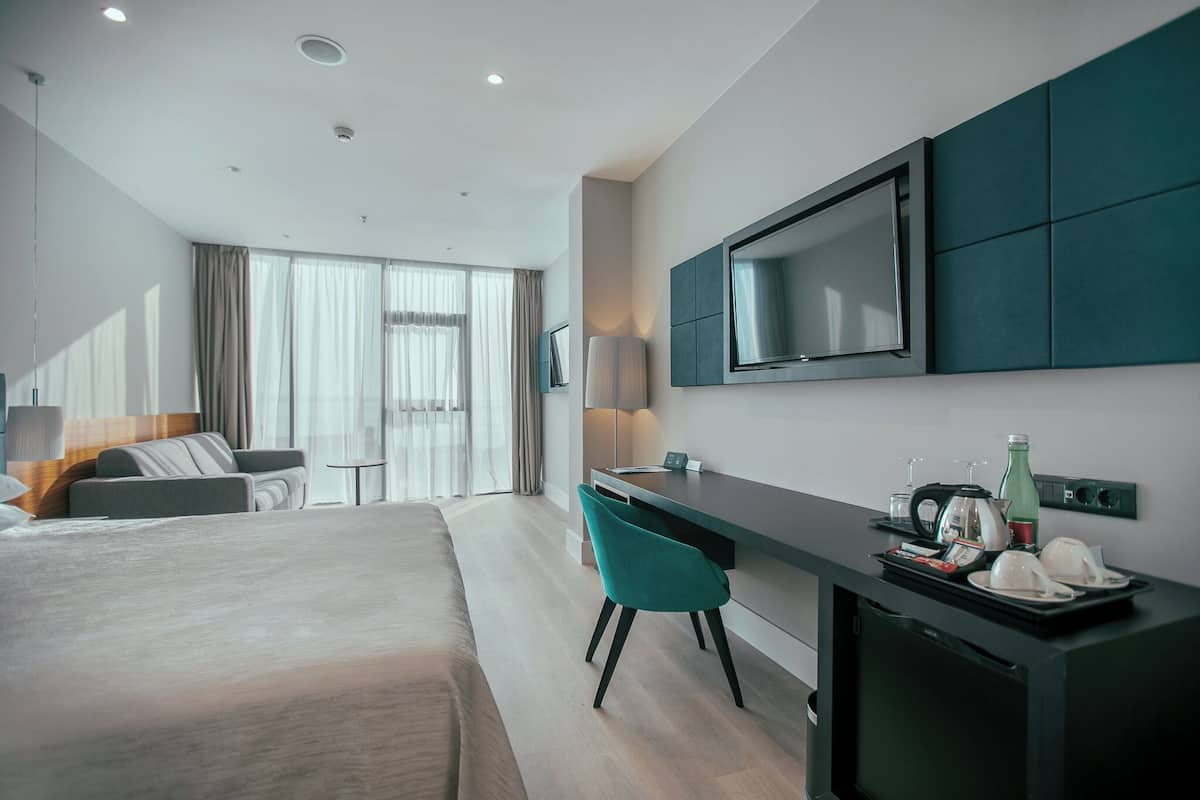 Una habitación de hotel moderna con una cama grande, un escritorio con una silla, un televisor de pantalla plana y un minibar.
