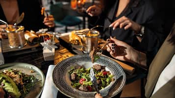 A dining table with various dishes, including a salad and a meat dish, and a person holding a fork.