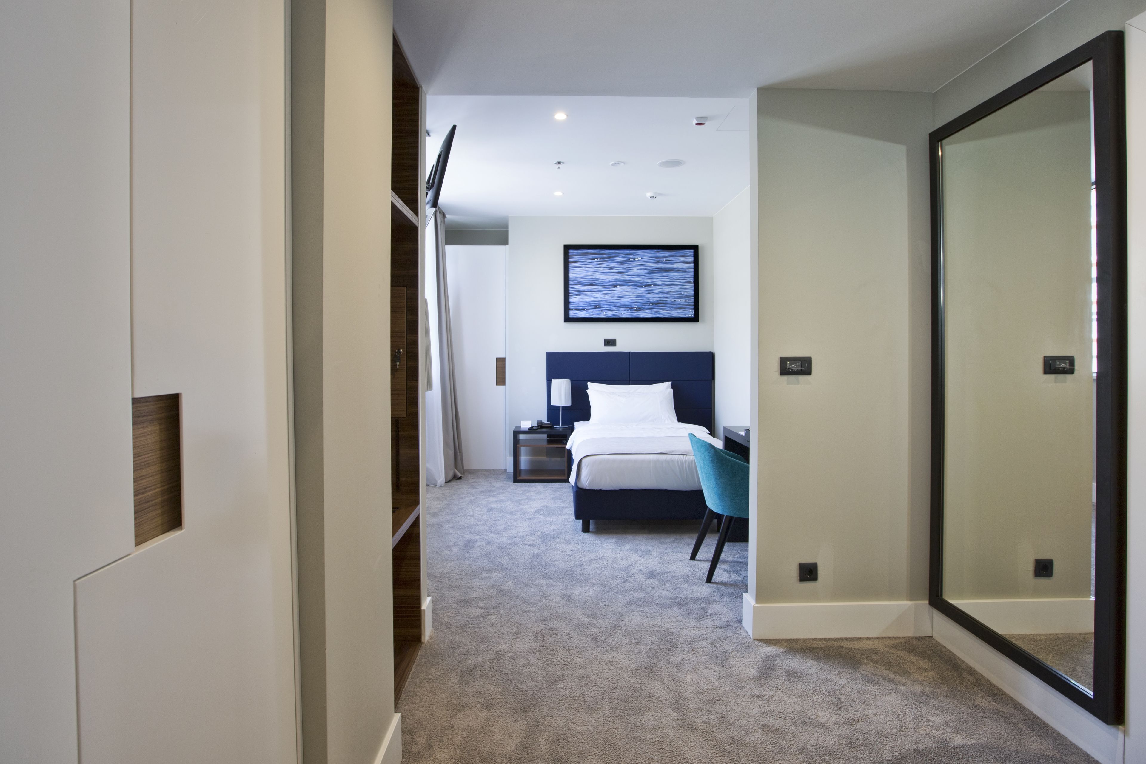 A modern hotel room with a large bed, a desk, and a chair. There is a TV mounted on the wall and a large mirror on one side.