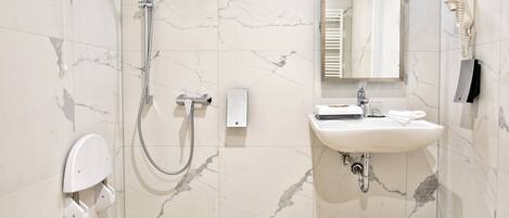 Un baño moderno con piso de mármol, ducha con cabezal de mano, inodoro con función bidé, lavamanos con espejo y dispensador de toallas.