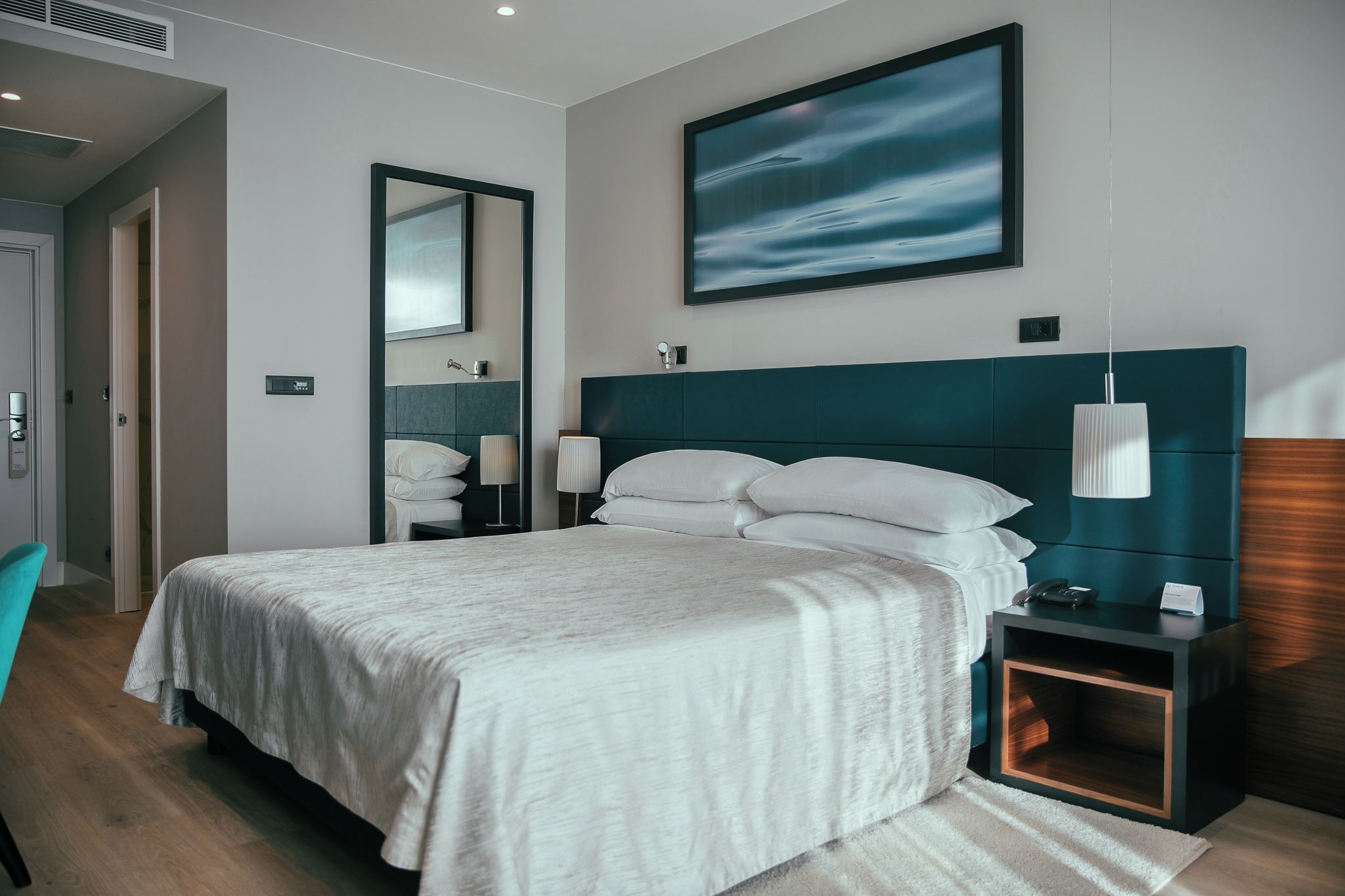 Habitación de hotel moderna con una cama grande, una mesita de noche, un espejo y un cuadro en la pared.