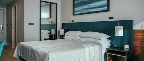 Habitación de hotel moderna con una cama grande, una mesita de noche, un espejo y un cuadro en la pared.