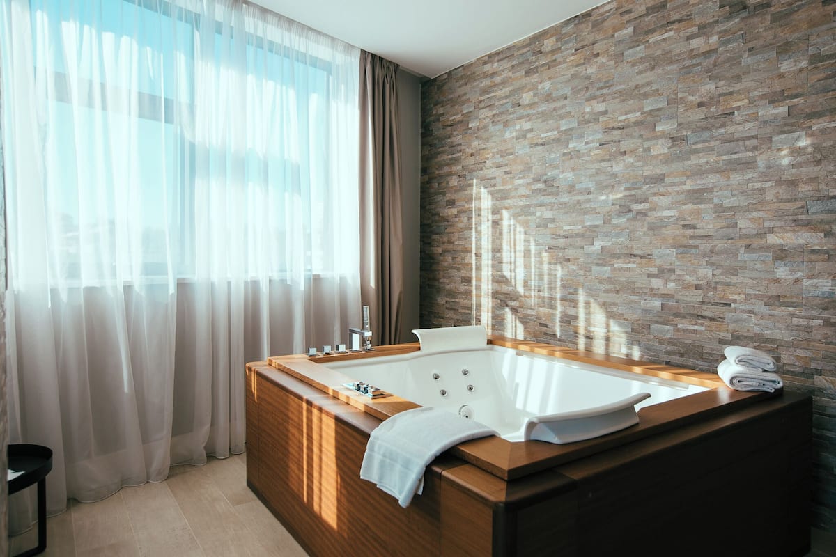 Un baño moderno con una bañera independiente, un tocador de madera y una pared con textura de piedra.