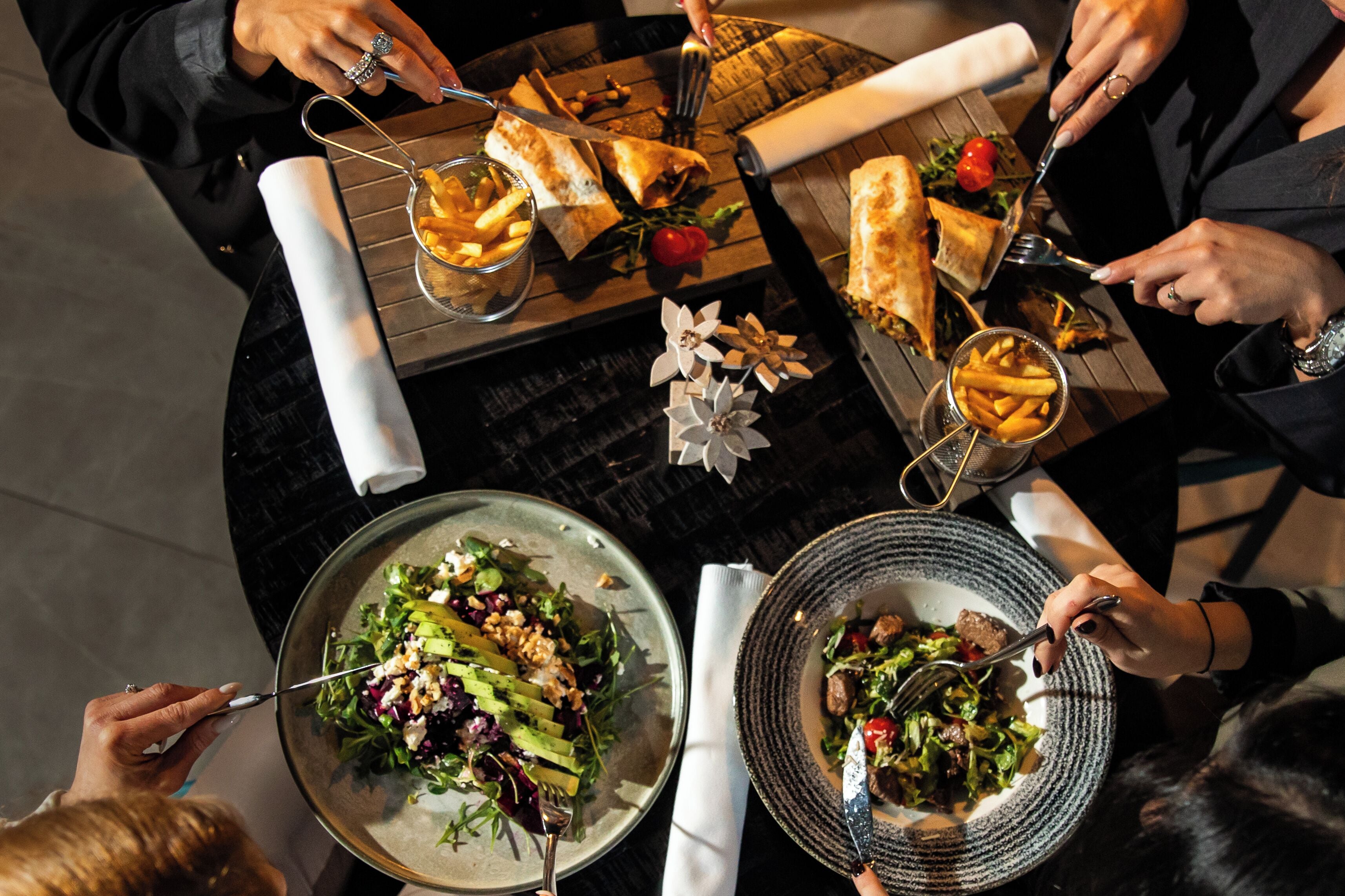 A dining table with various dishes, including a salad, sandwiches, and a bowl of fries.