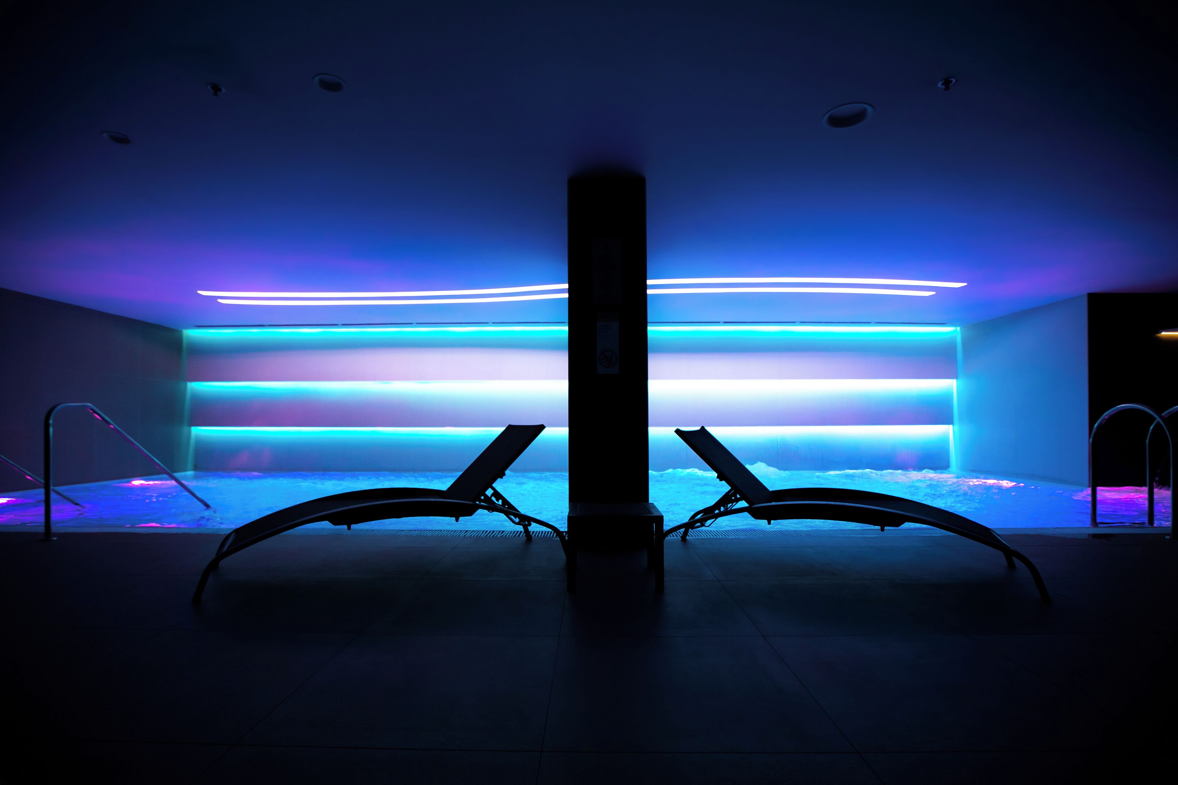 Zona d'spa amb dues gandules i una piscina, il·luminada per llums blaves i púrpures.