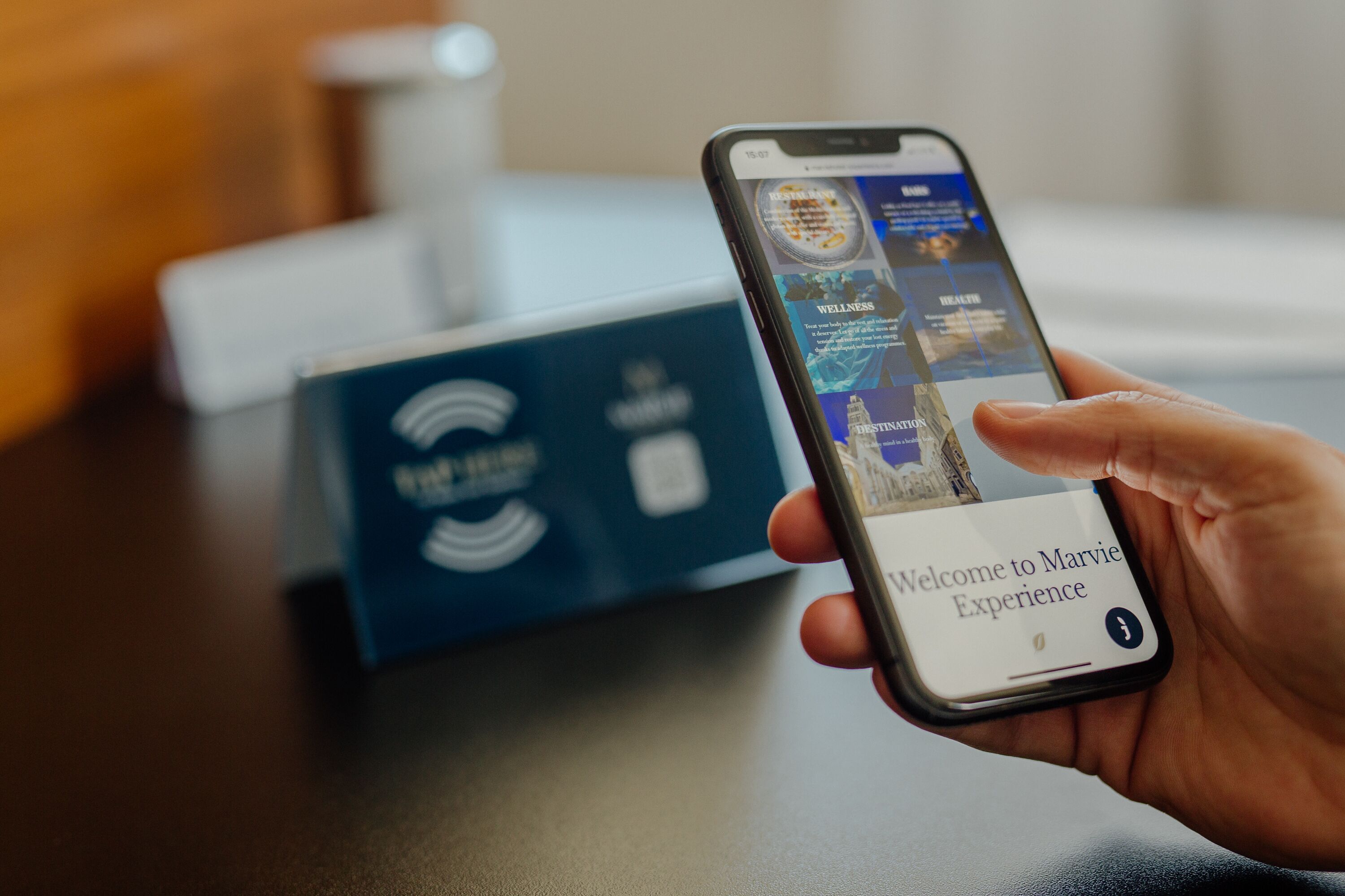 A hand holding a smartphone displaying a welcome screen for Marvie Experience.
