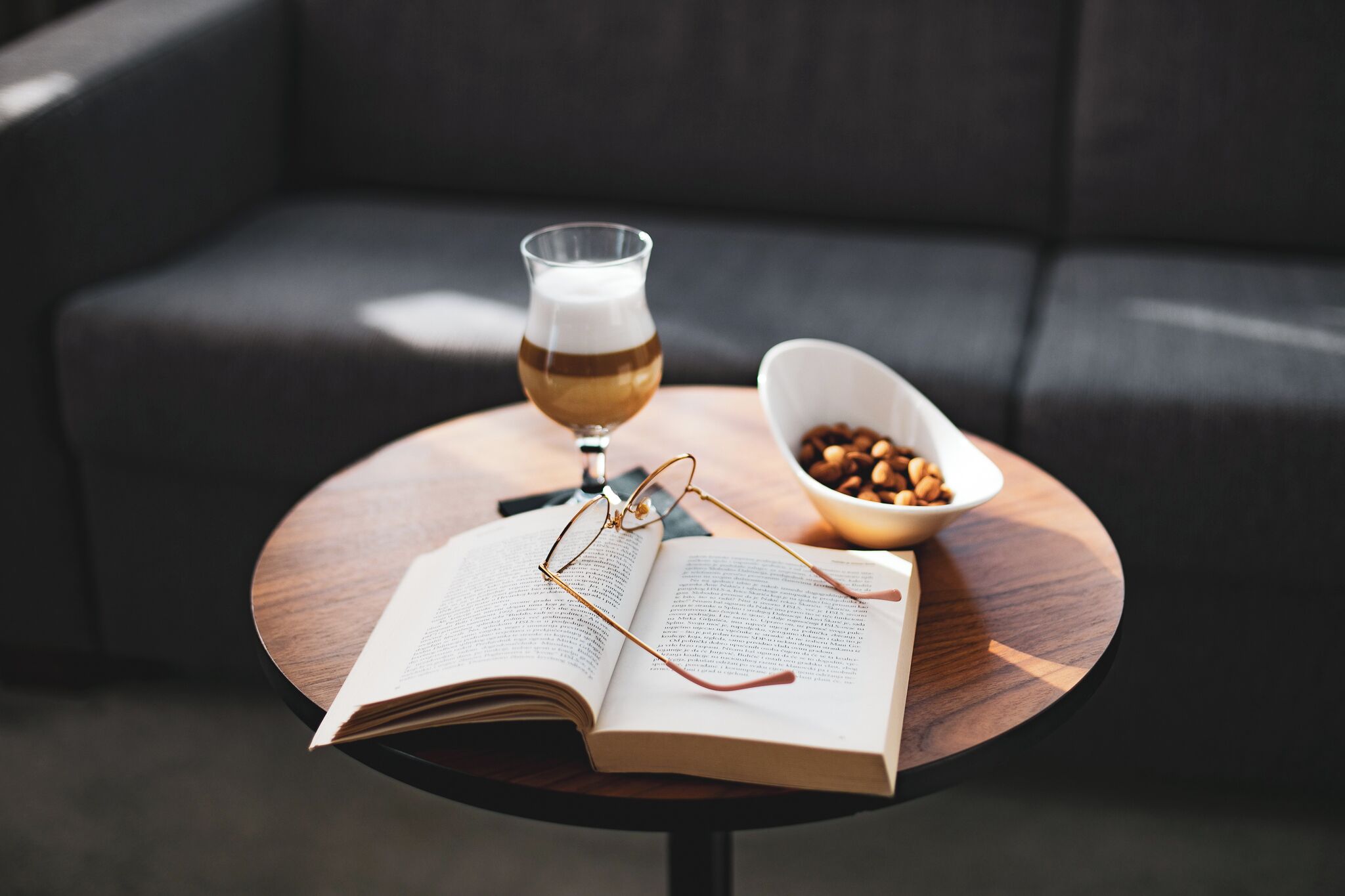 An open book on a round wooden table with a glass of beer and a bowl of nuts.