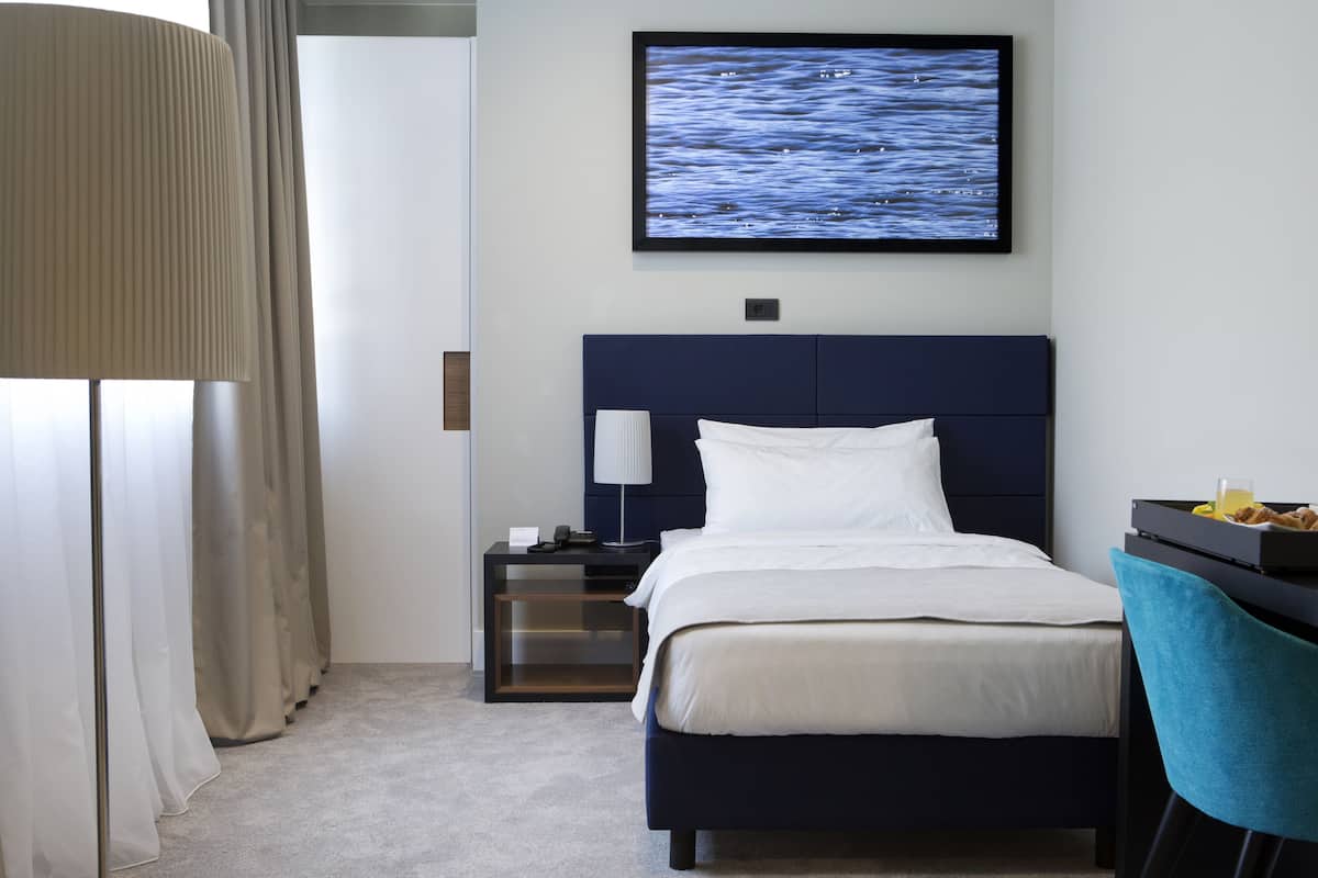 Habitación de hotel con cama, mesita de noche, televisor, lámpara, silla y escritorio con una bandeja de comida.