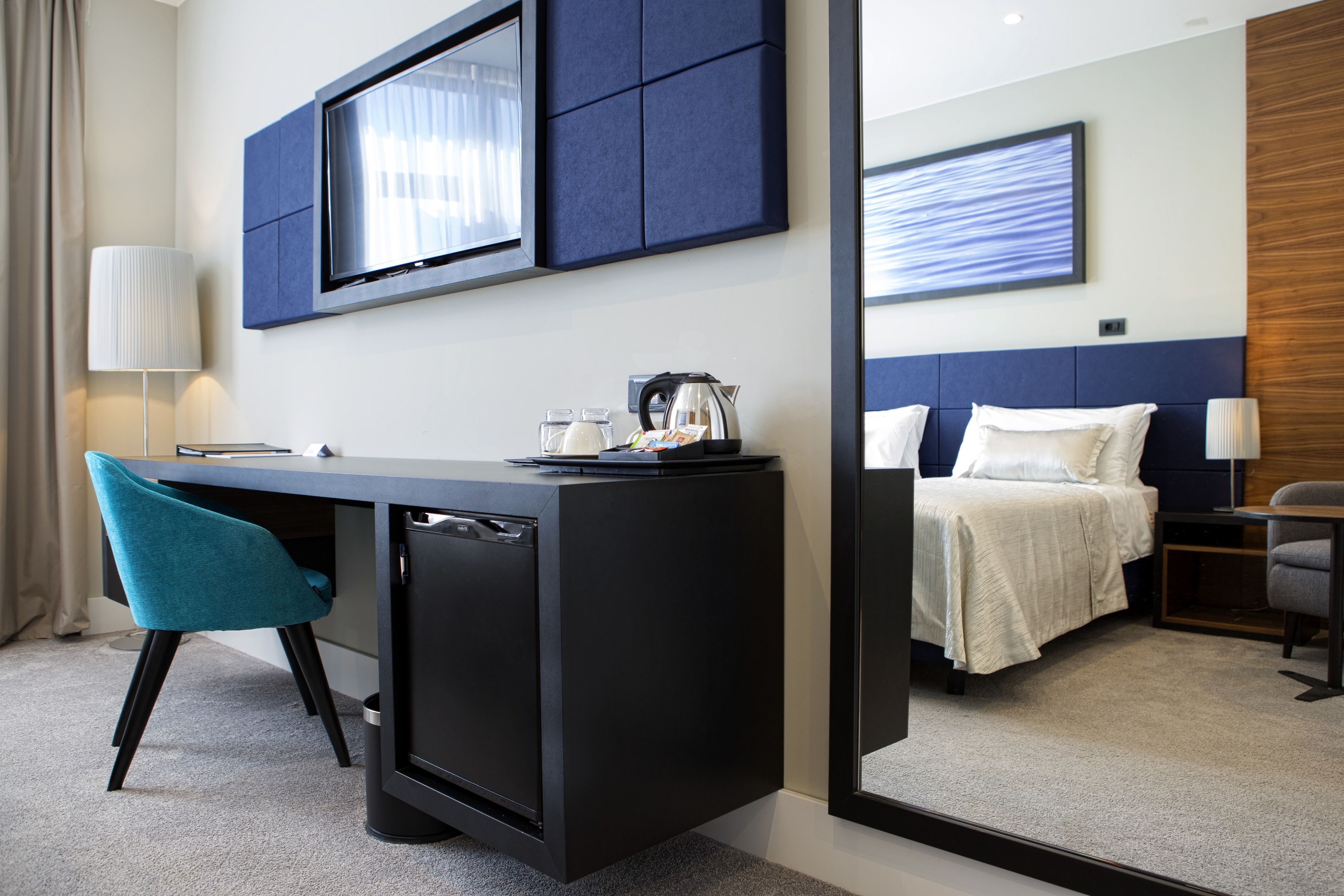 Una habitación de hotel con escritorio, una silla, una cama, televisor y cafetera.