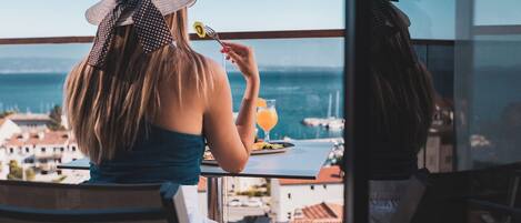 A person dining at a table with a view of the sea and buildings in the background.