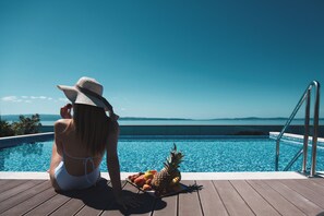 A woman sitting by a pool with a pineapple and fruits, overlooking a clear blue sky and water. - Marvie Hotel & Health (Split)