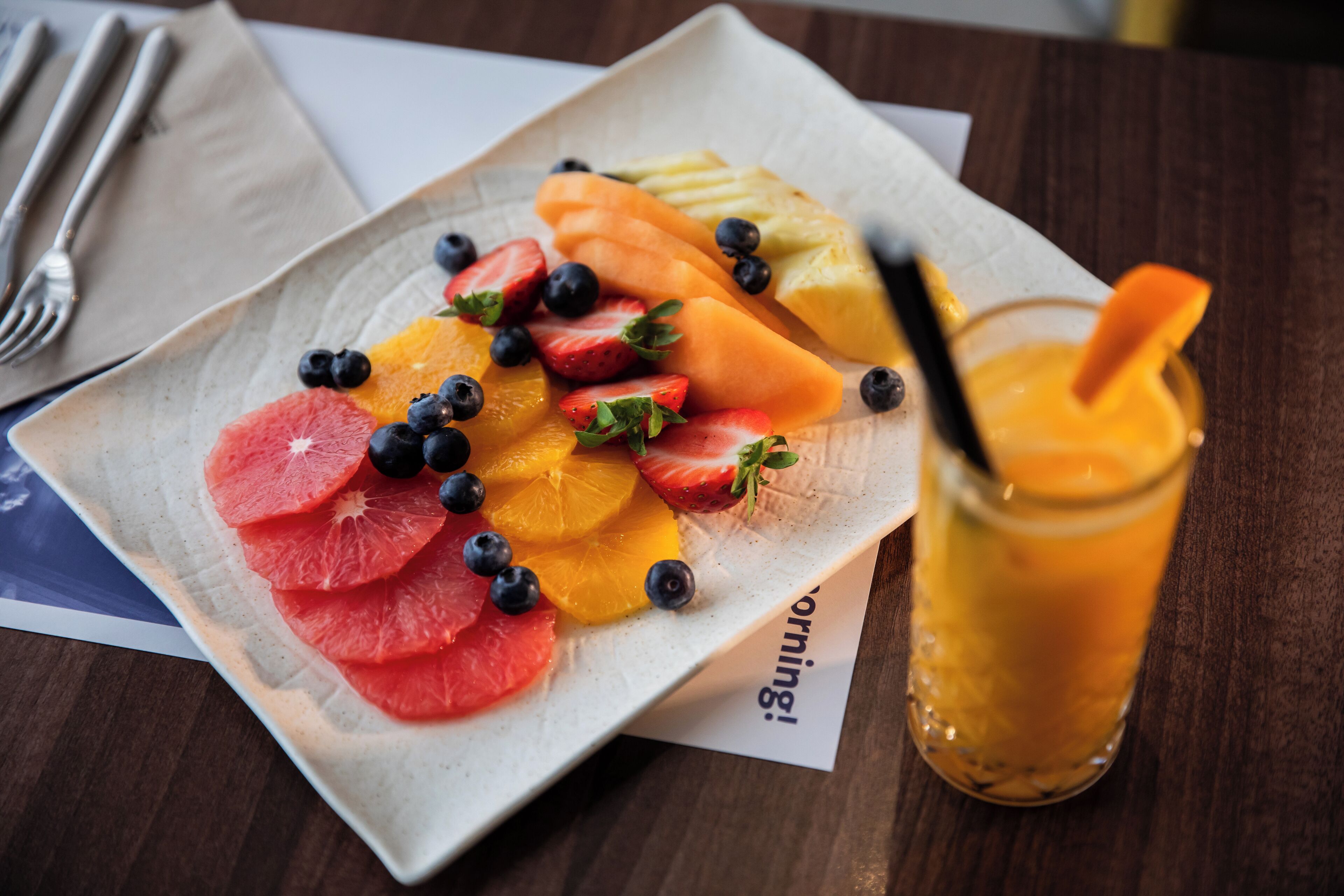 Un plato de frutas cortadas y un vaso de jugo de naranja sobre una mesa.