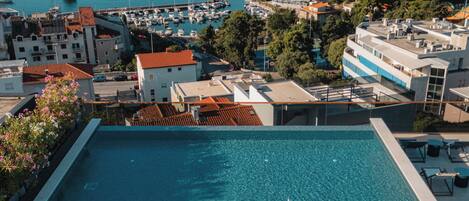 A rooftop pool with clear blue water, surrounded by lounge chairs and a view of the sea and marina.