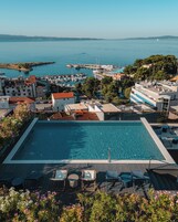 A rooftop pool with clear blue water, surrounded by lounge chairs and a view of the sea and marina.
