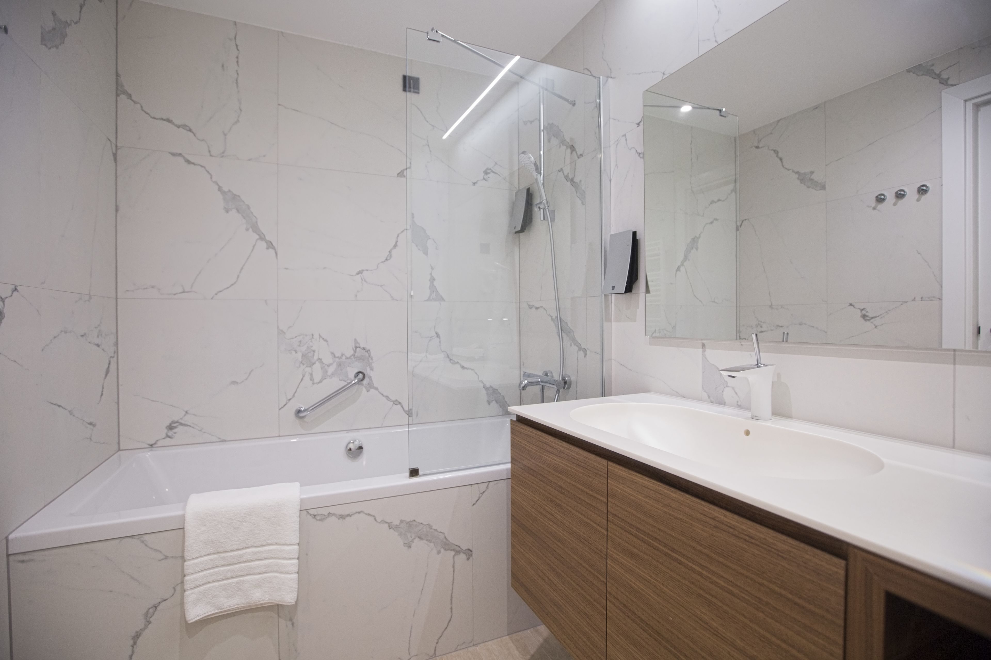 Ein modernes Badezimmer mit Marmorwand, einer Badewanne, einem großen Spiegel und Holzschränken.