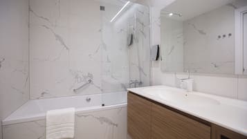 A modern bathroom with a marble wall, a bathtub, a large mirror, and wooden cabinets.