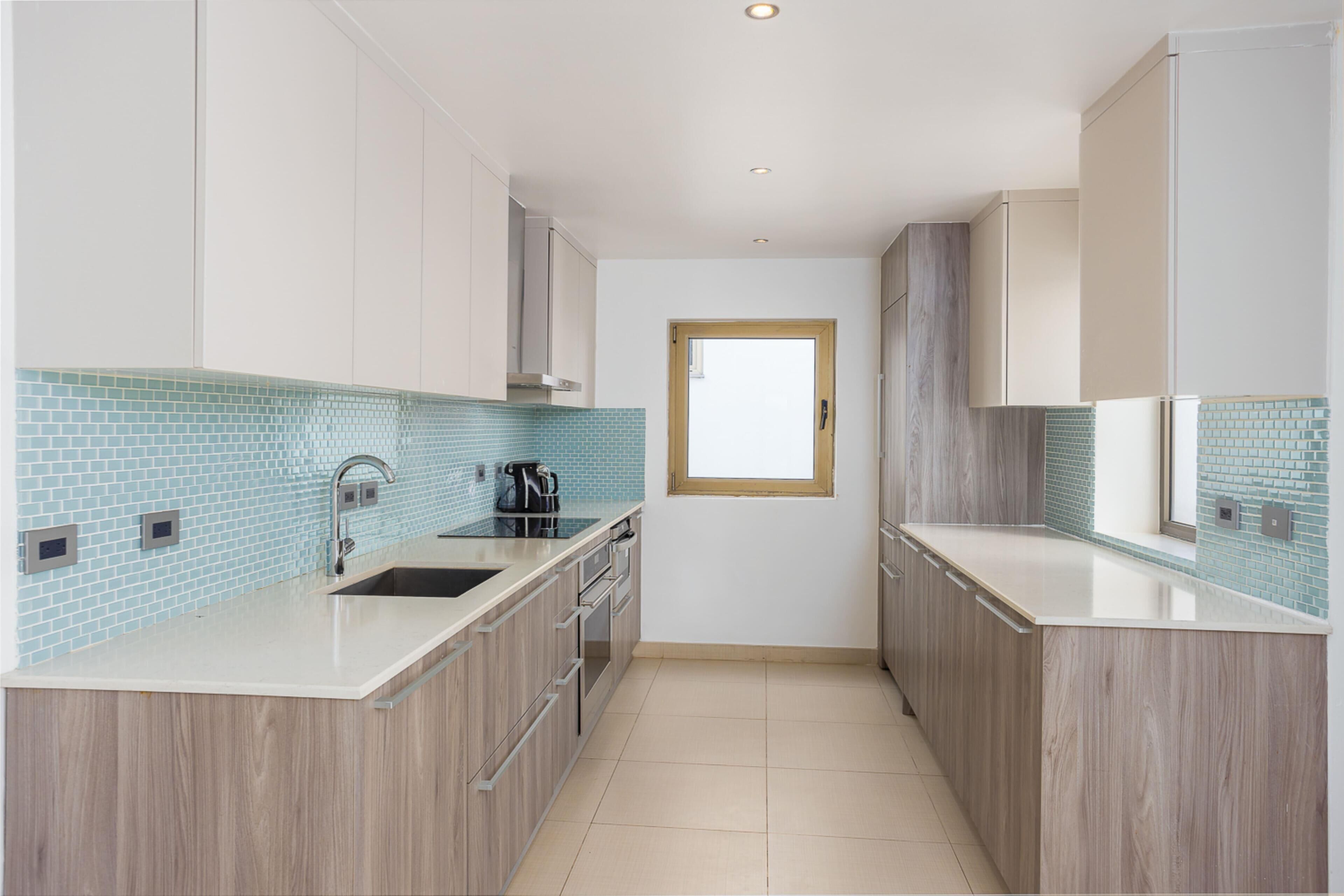 Una cocina moderna con armarios de madera clara, encimera blanca y salpicadero de azulejos azules.