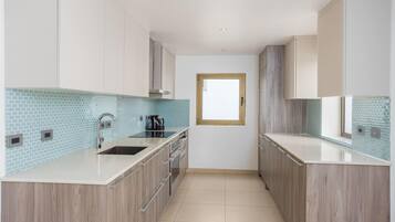 Una cocina moderna con armarios de madera clara, encimera blanca y salpicadero de azulejos azules.