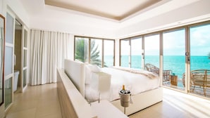 Un dormitorio moderno con una cama grande, vista al mar y un balcón con sillas de mimbre.