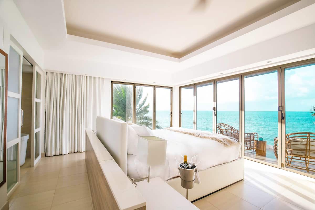 A modern bedroom with a large bed, a view of the sea, and a balcony with wicker chairs.